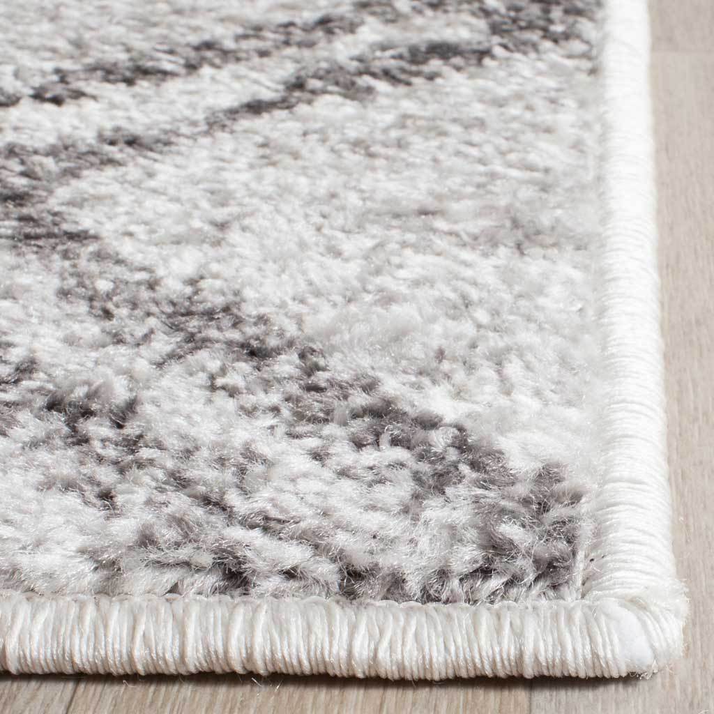 Soft silver and charcoal fibers meet a neatly wrapped edge at the rug's corner
