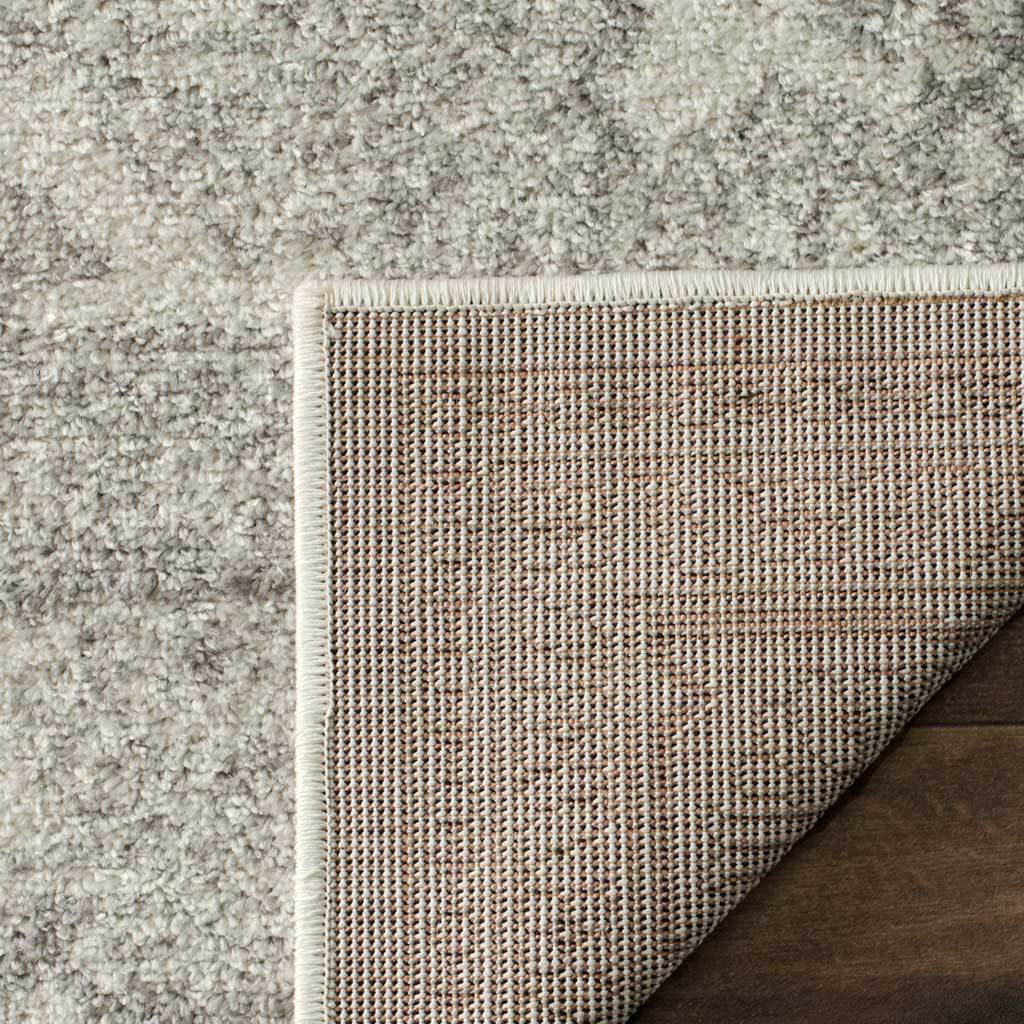 A folded ivory and silver rug corner exposes tightly woven backing and a bound edge.
