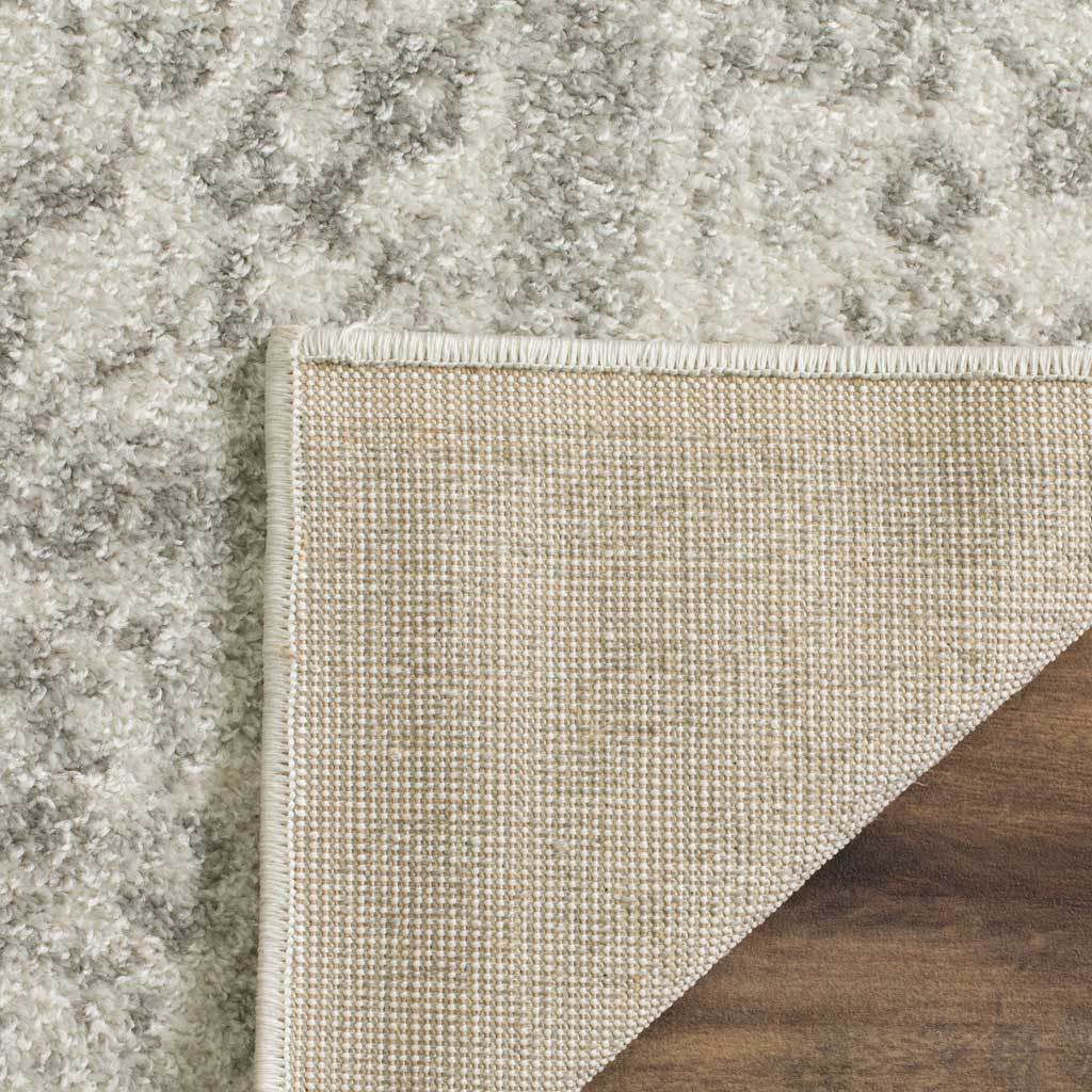 A bound corner lifts to show the woven reverse of this ivory and silver rug.