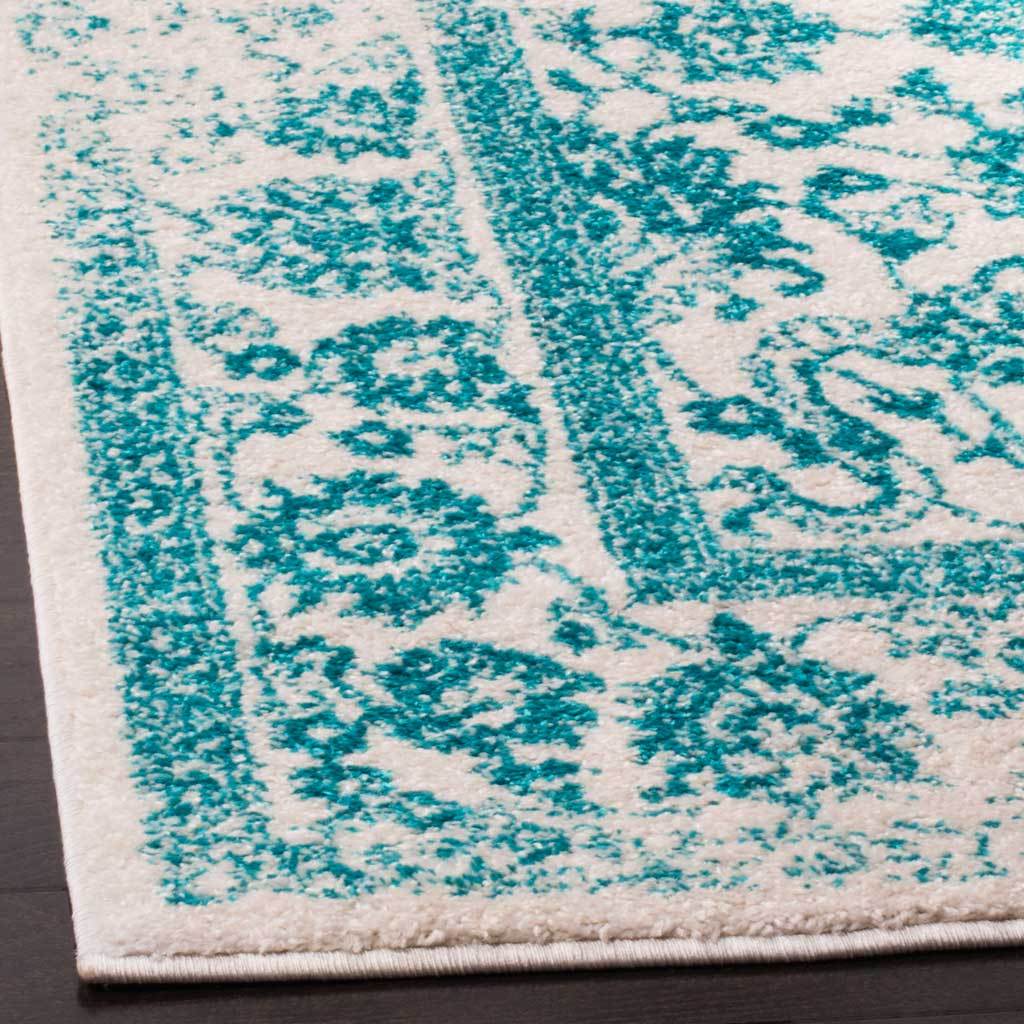 Teal botanical flourishes contrast with ivory pile along the rug's bound edge.