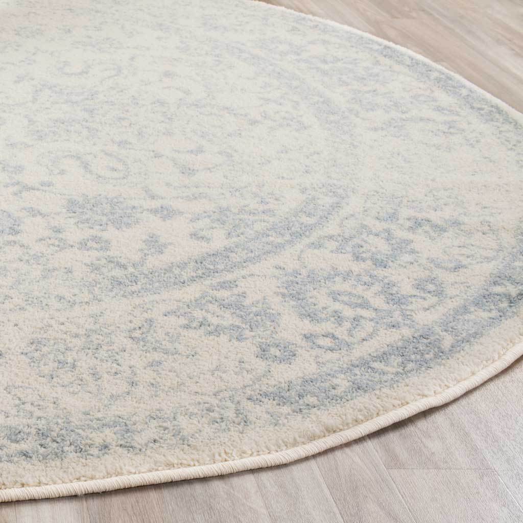 Slate florals soften across ivory pile, finished with a neatly bound curved edge