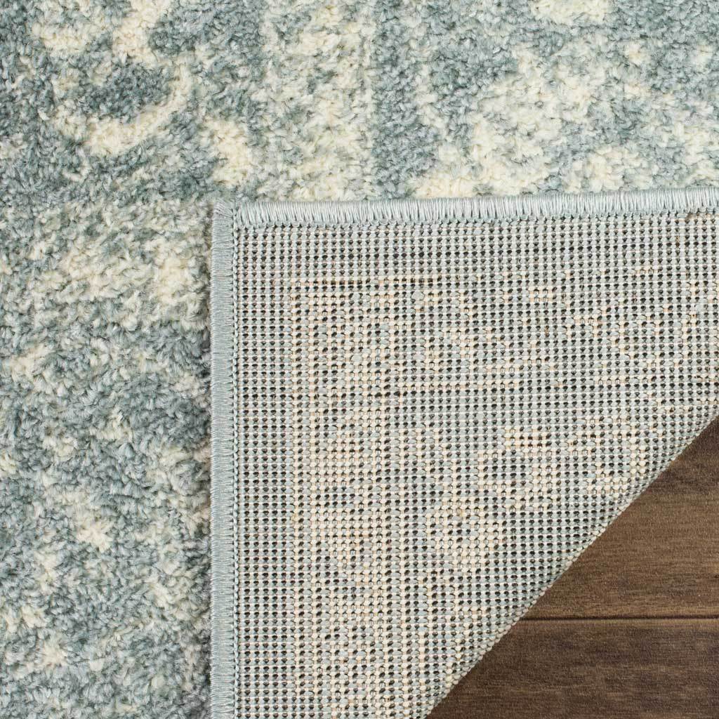 A neatly bound corner reveals woven backing beneath the slate-and-ivory pile.