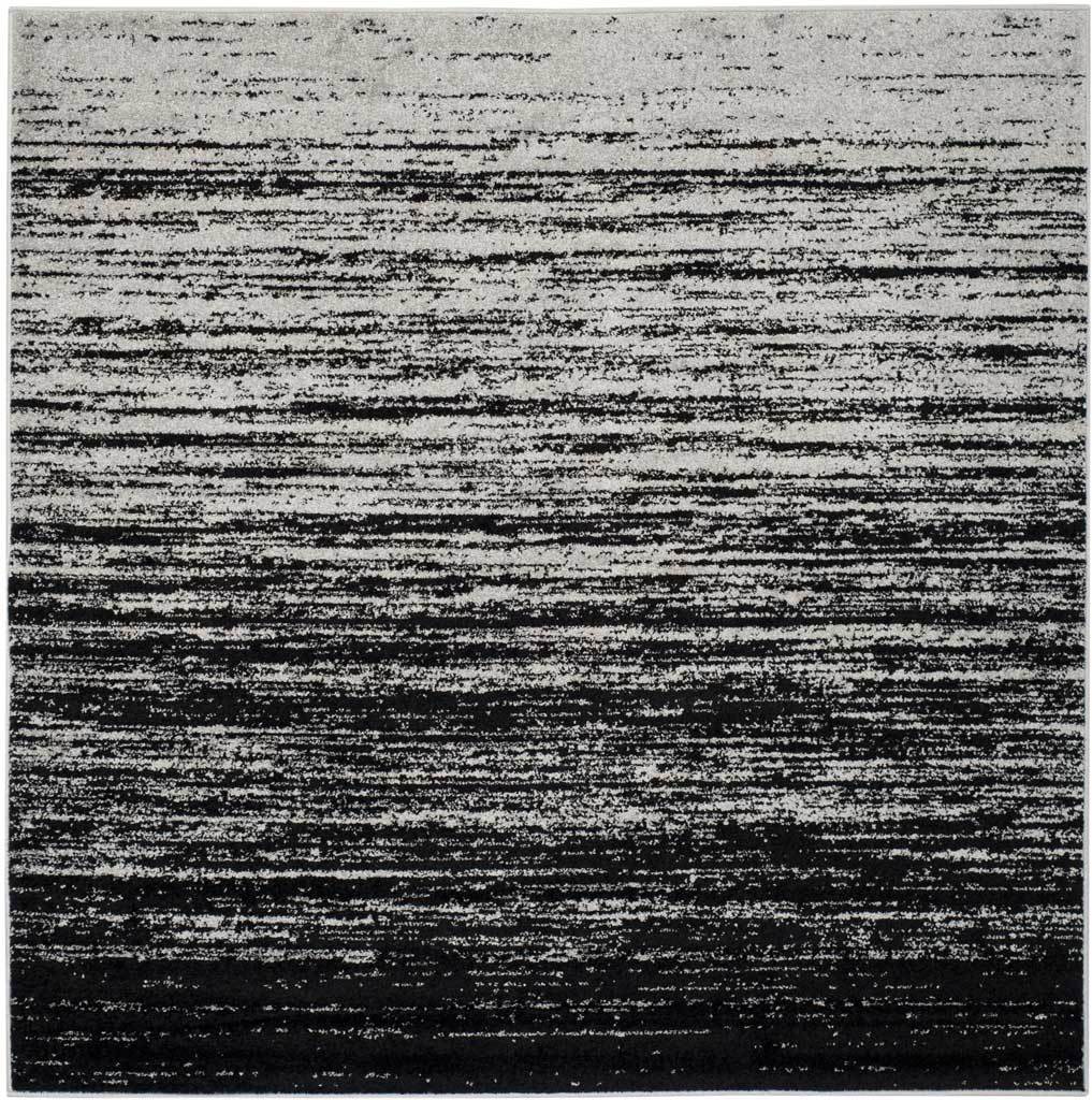 A square silver-and-black rug layers bold dark bands over a weathered pale field.