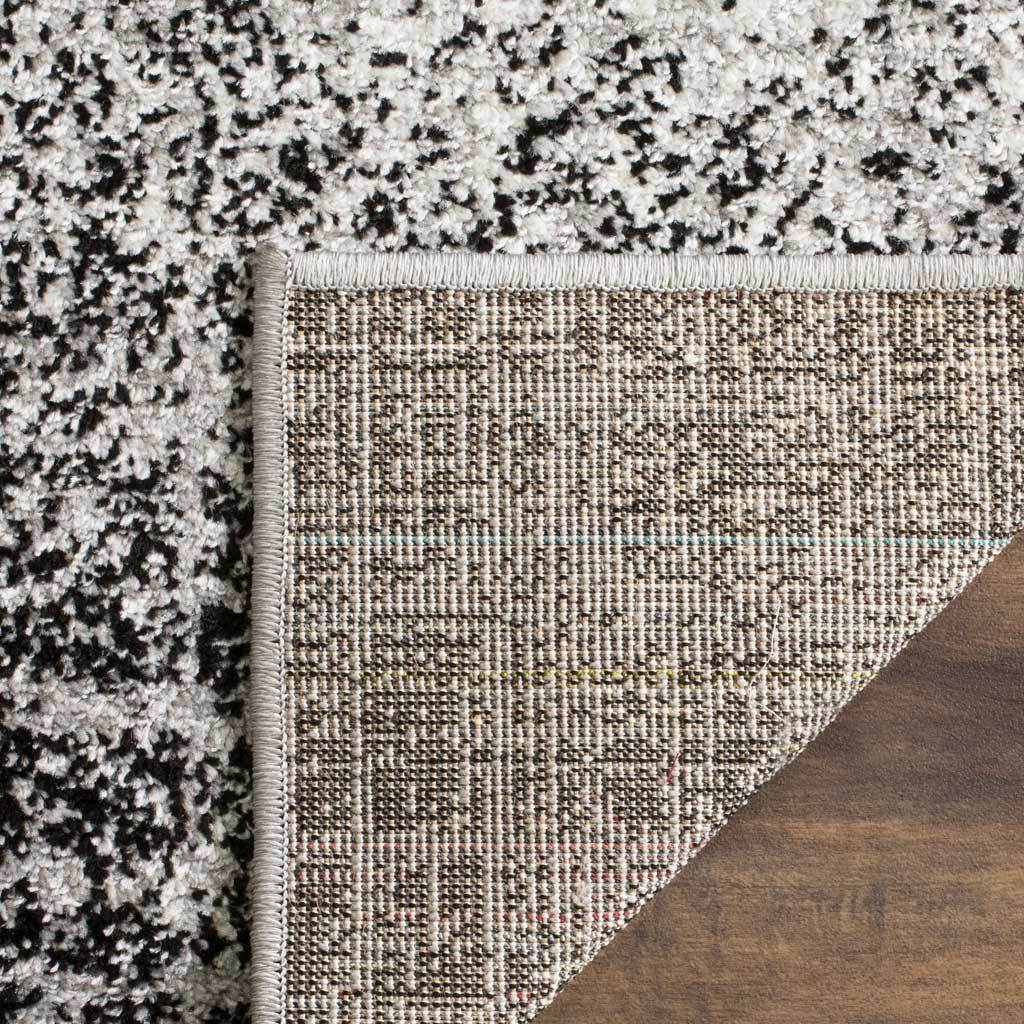 Woven jute backing with tidy binding contrasts with the rug's mottled silver and black pile