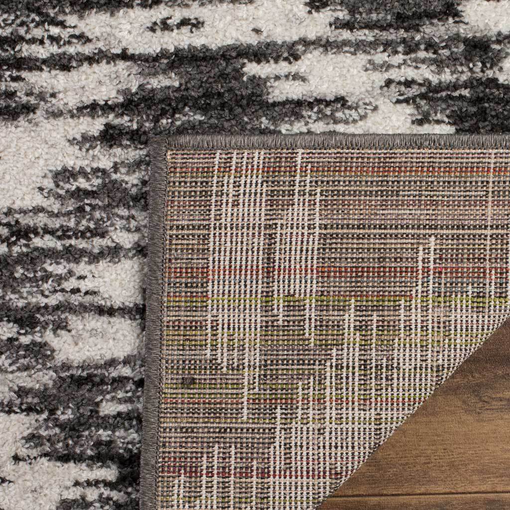Woven grid backing and a finished edge support the charcoal and ivory patterned rug
