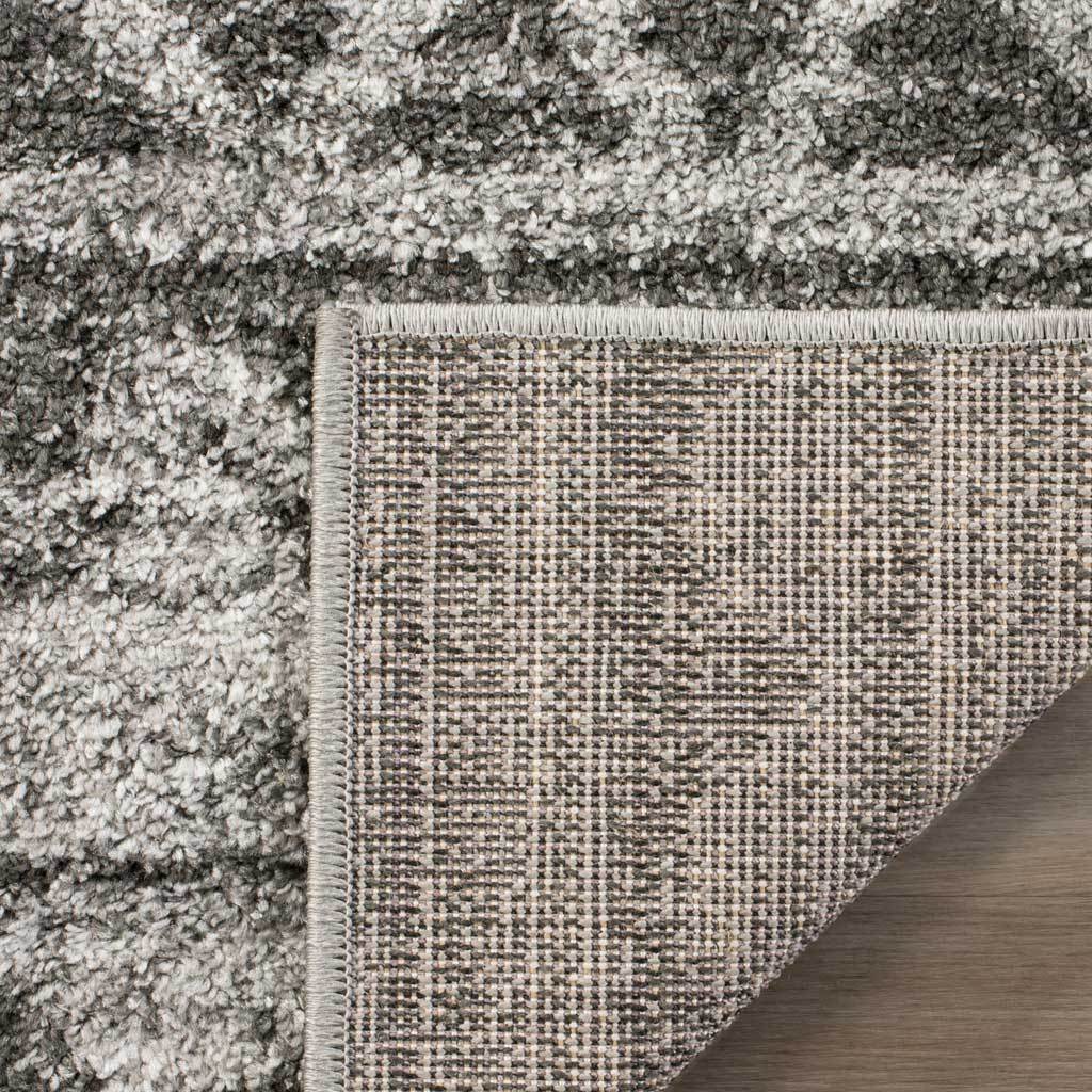 A folded corner reveals woven backing beneath the rug's textured charcoal-and-ivory pile.