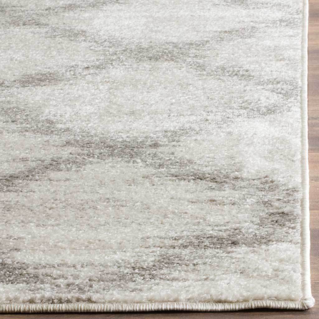 A clean stitched border finishes the ivory and silver pile with gentle shading throughout