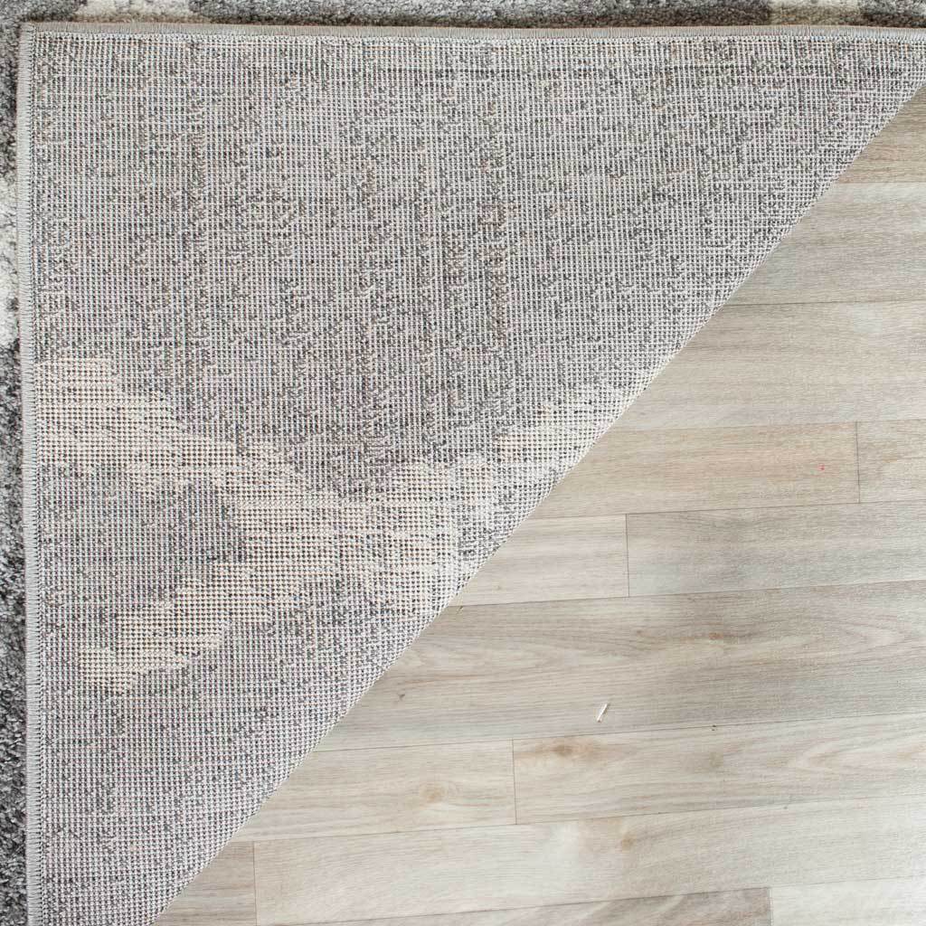 A tightly woven backing and finished edge support the rug's silver-gray patterned pile.