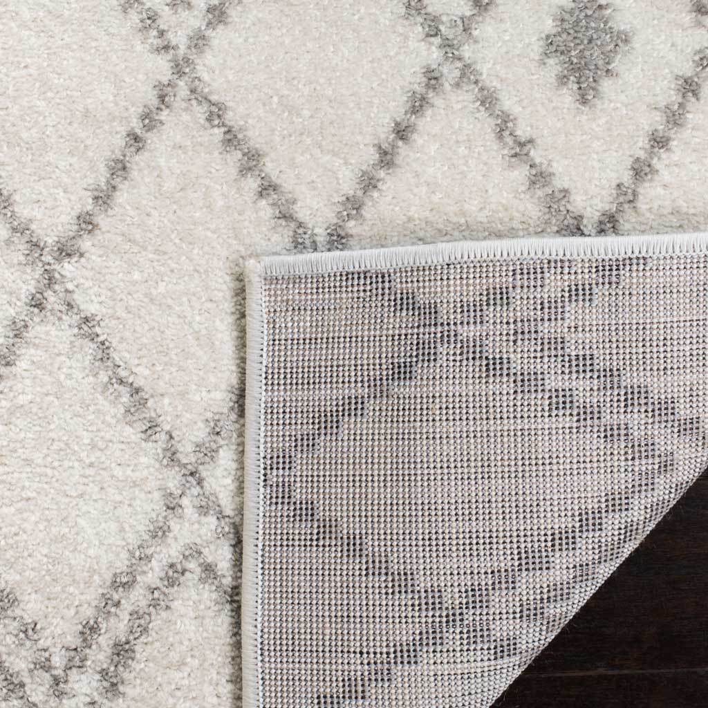 A folded corner reveals woven backing beneath the ivory and gray patterned pile.