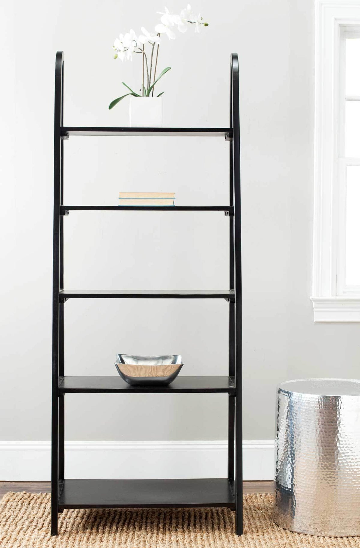 An airy black etagere displays flowers, books, and a bowl across its graduated shelves.