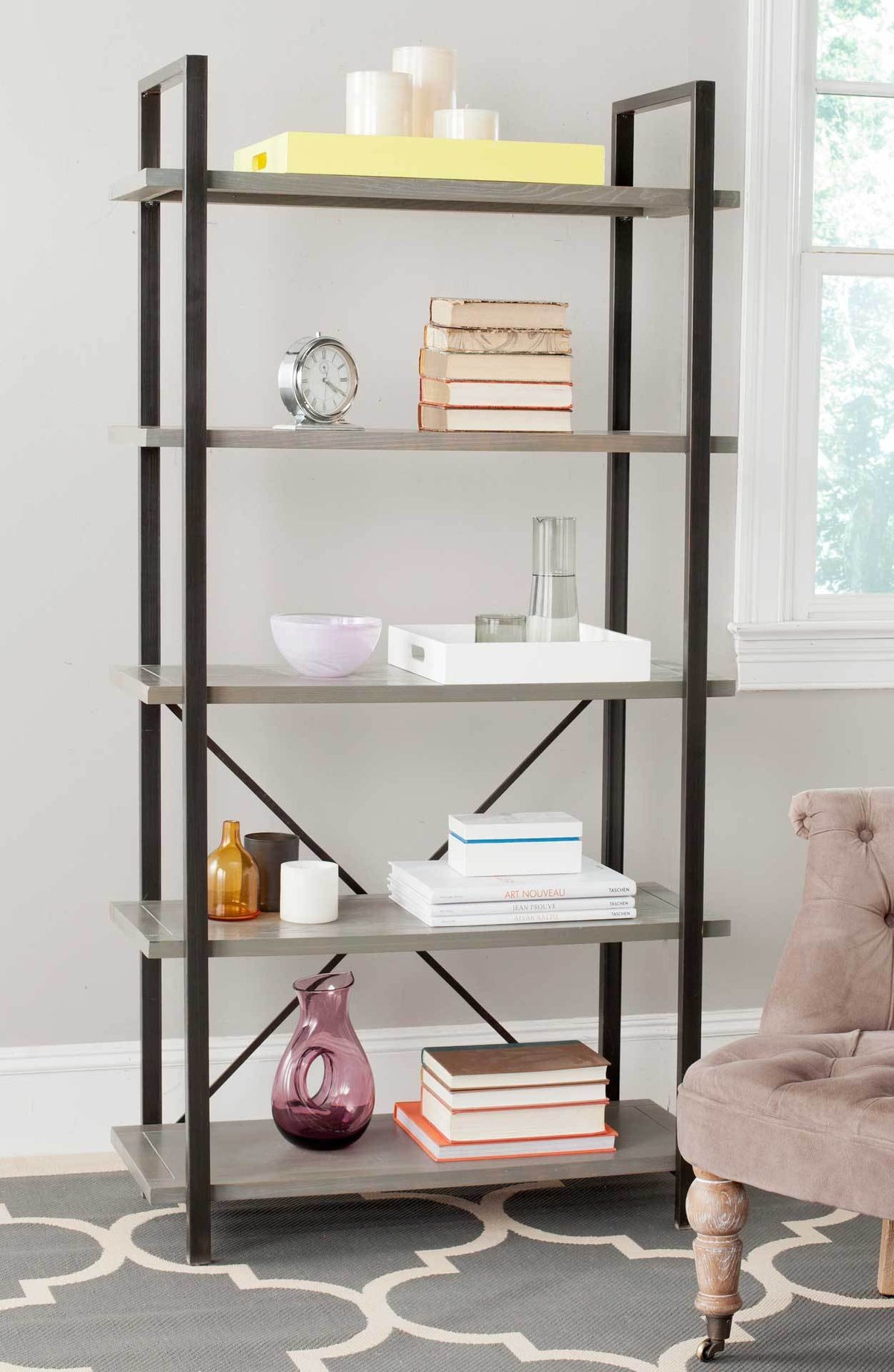 Airy gray wood shelves hold books and decor within a black iron frame.