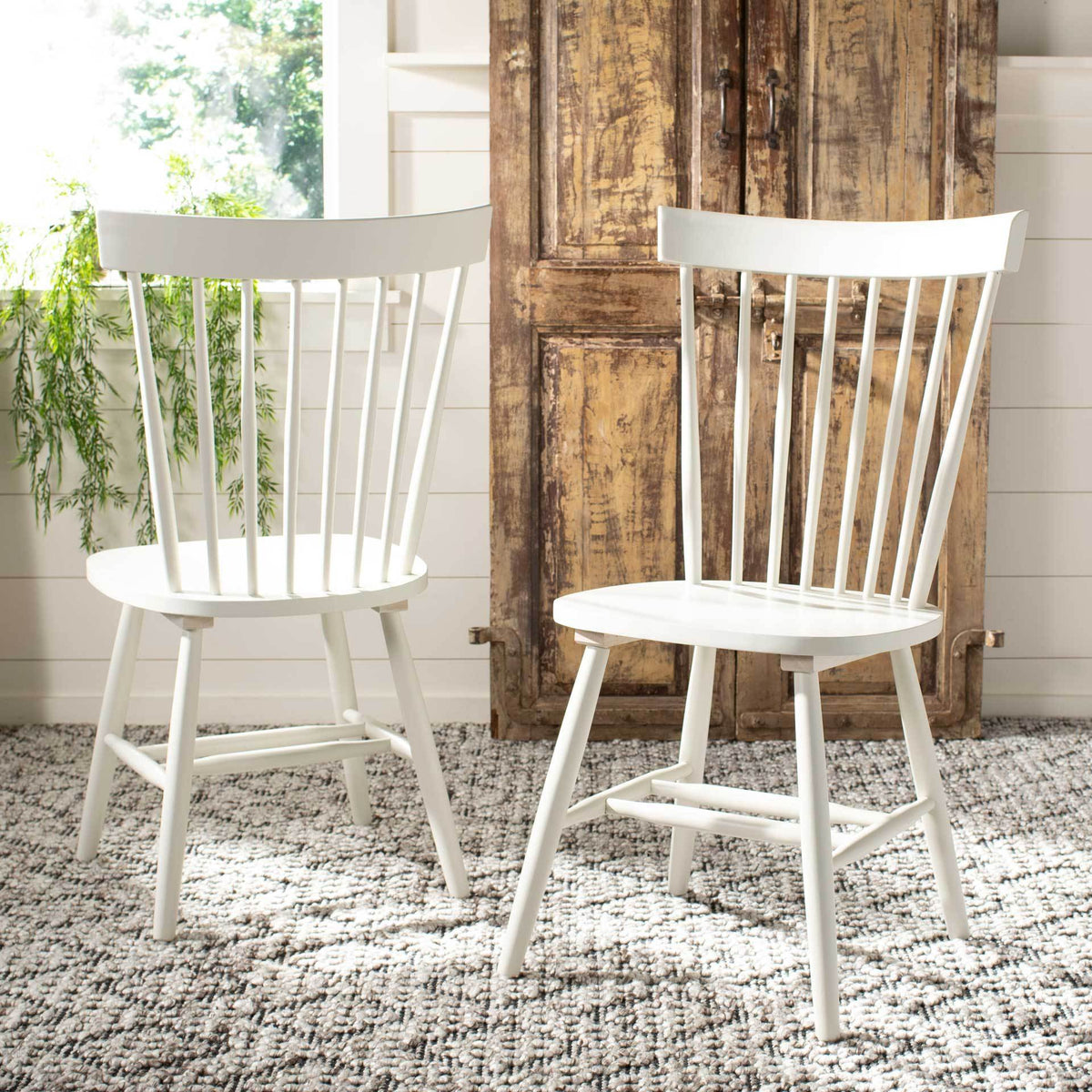 An off-white pair of spindle-back chairs stands out against rustic wood and a textured rug.