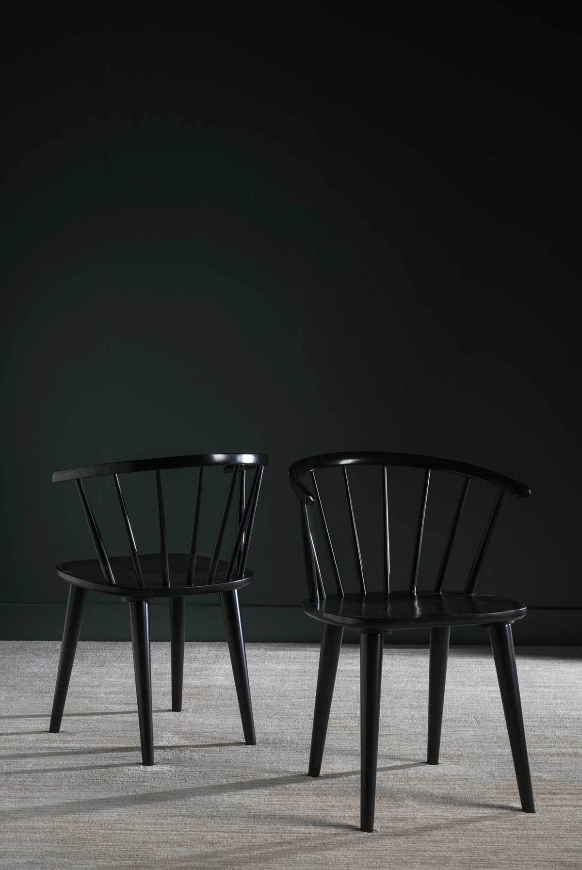 Two black chairs pair sculptural curved backs with slim legs against a moody wall.