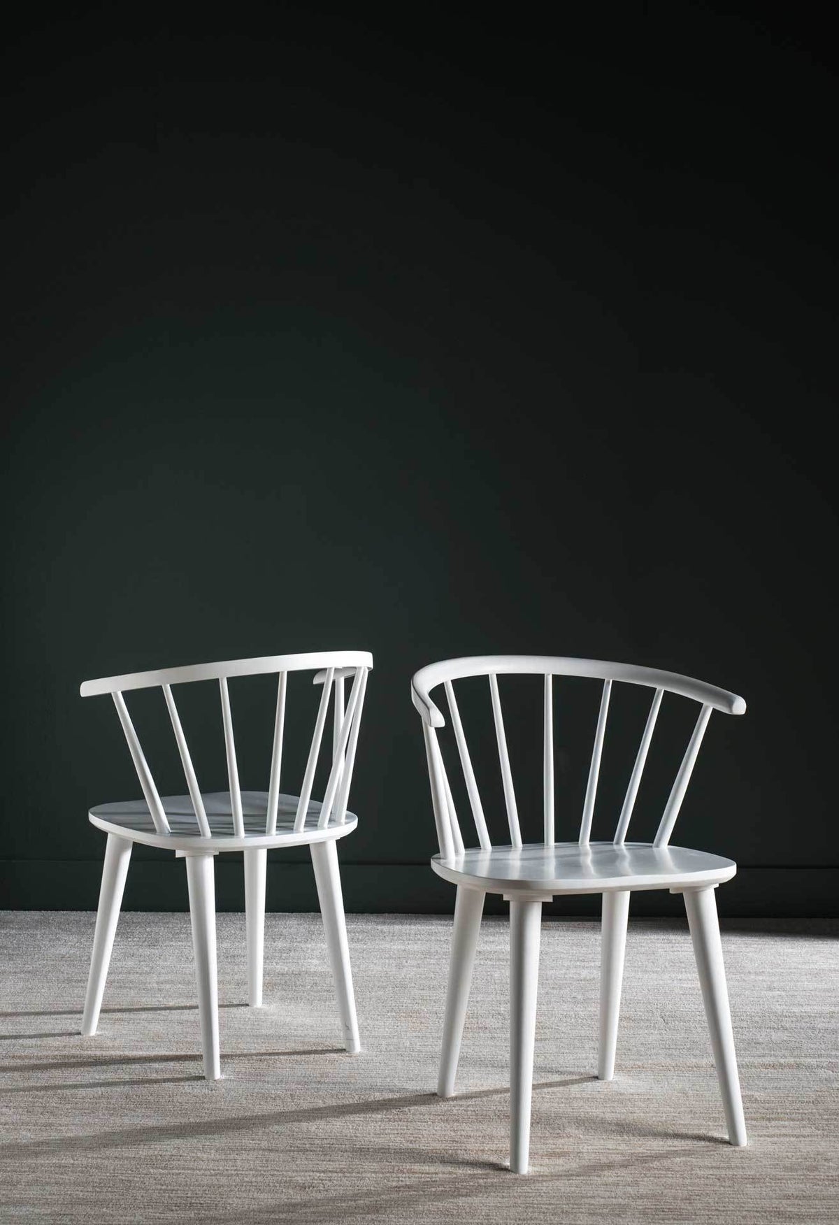 Two white wood chairs brighten a dark-walled space with airy spindle backs.