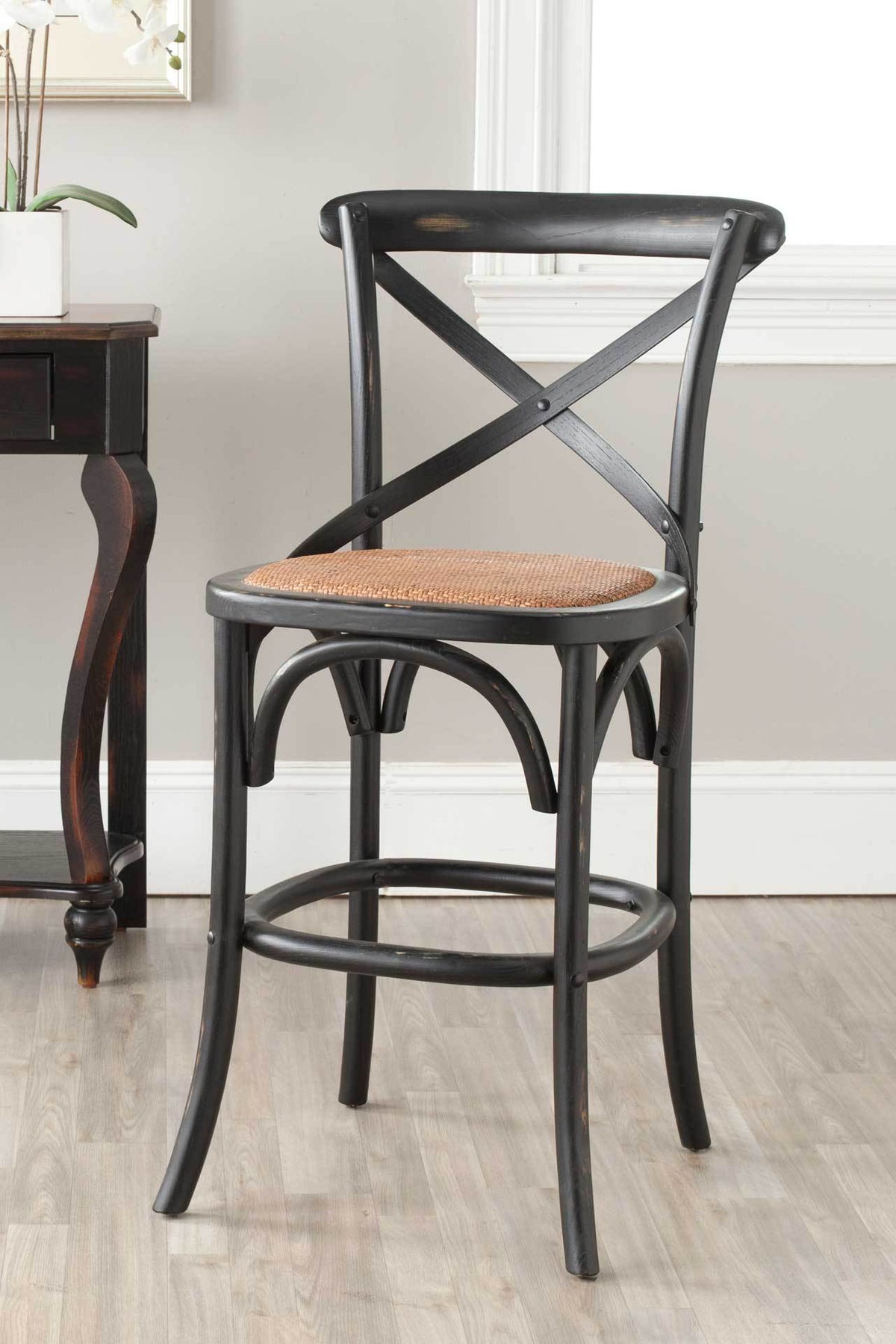 A black X-back stool brings rustic texture with its rattan seat and circular footrest