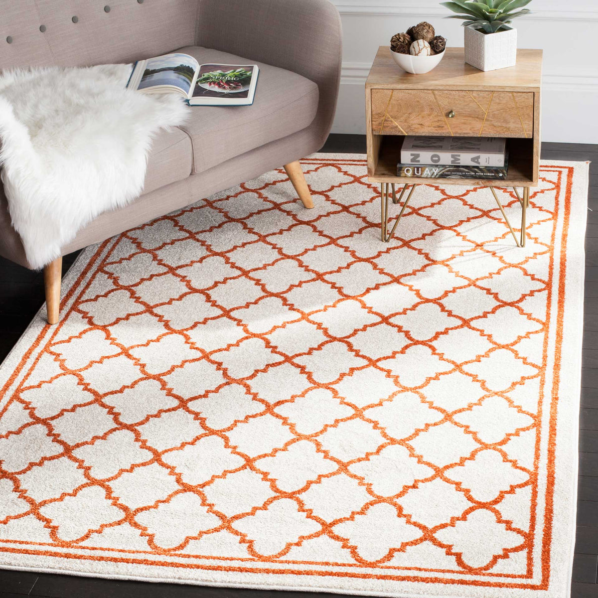 A vibrant orange trellis warms the beige rug beneath a curved sofa and wood side table.