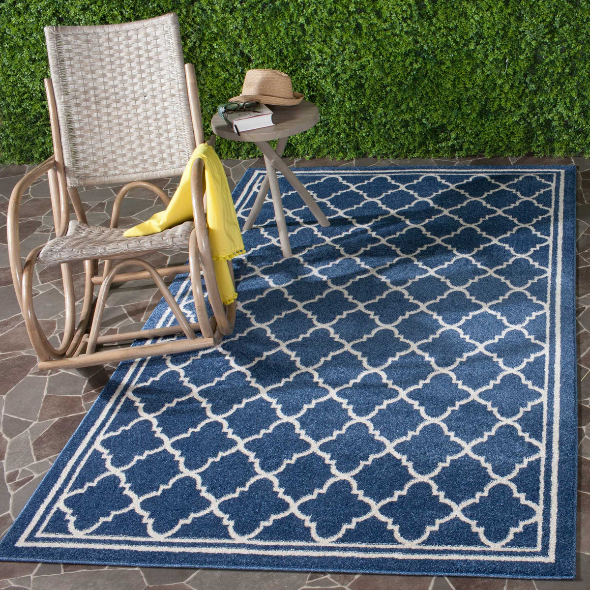 A navy rug with a beige trellis grounds a patio seating area beside a woven chair.