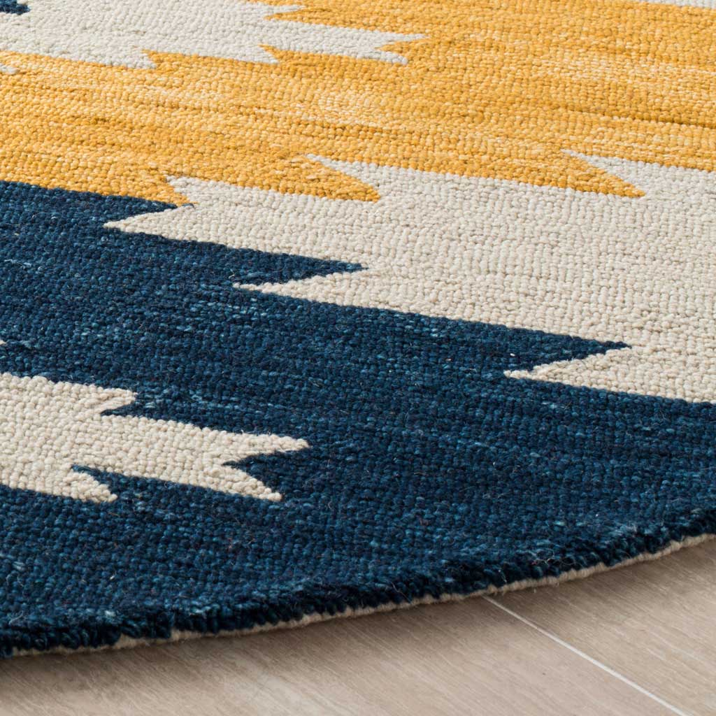 Textured wool pile and a curved finished edge accent navy, ivory and golden yellow zigzags.