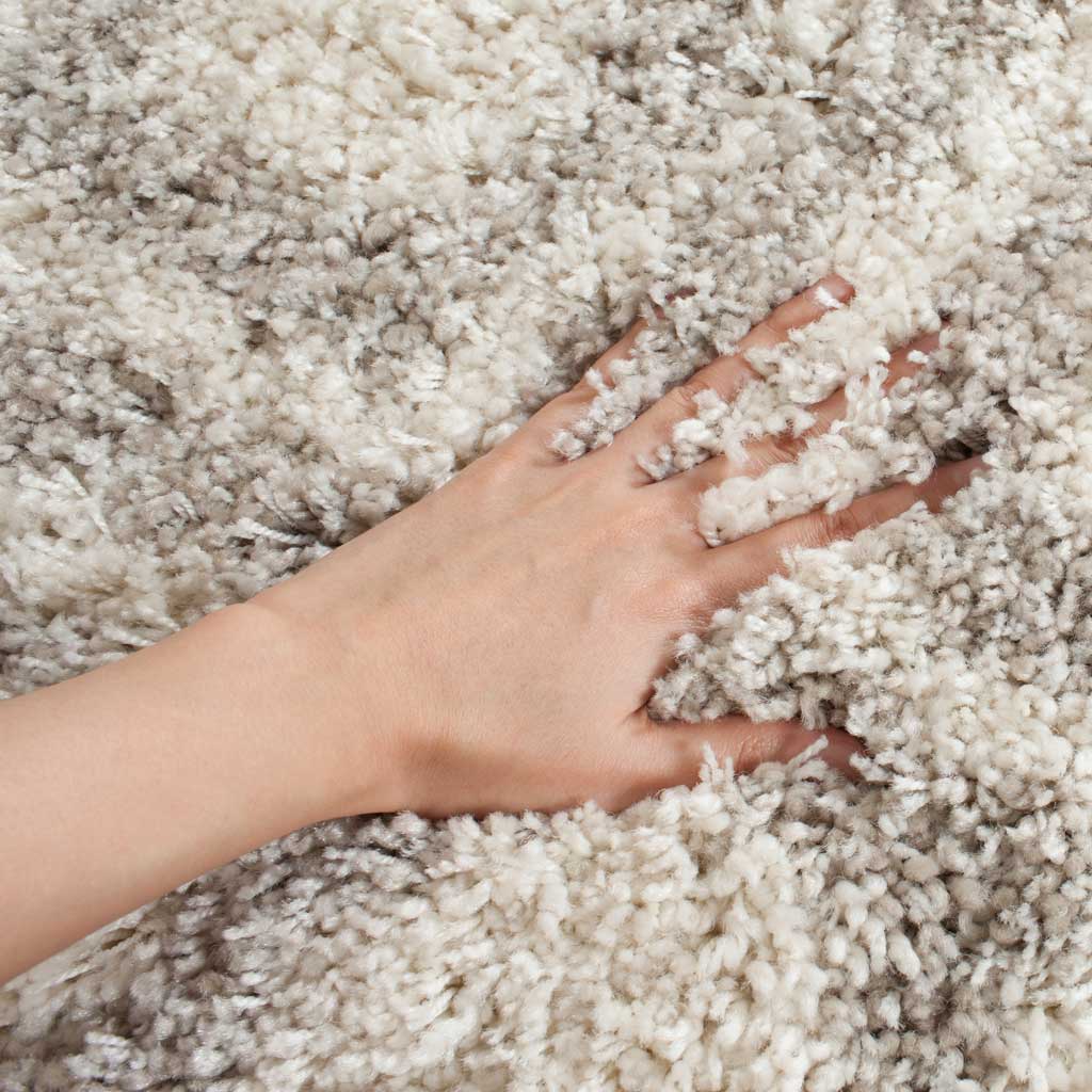 A hand settles into fluffy ivory and beige fibers, revealing the rug's generous pile.