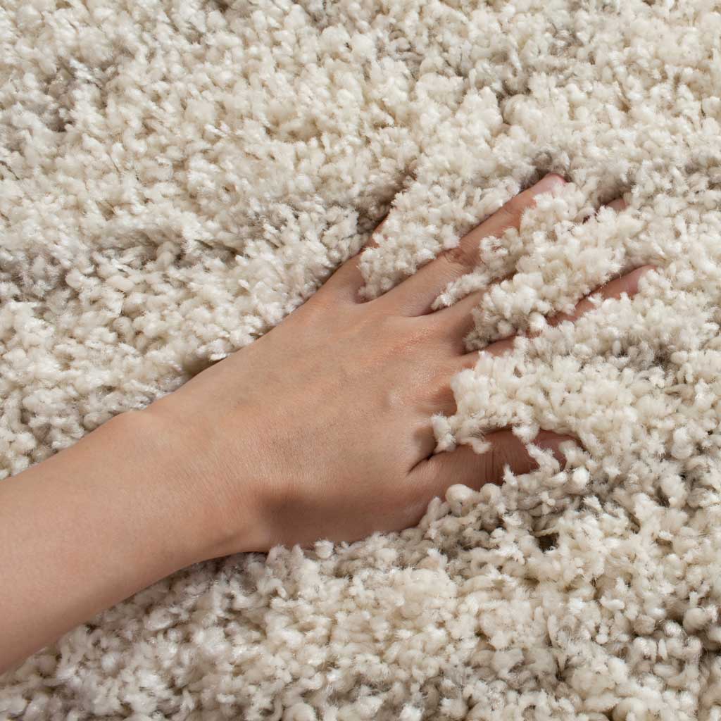 A hand disappears into dense ivory shag, revealing a soft, cushiony texture.