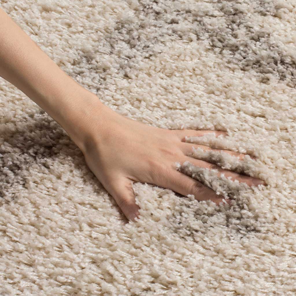 A hand presses into the soft ivory and gray pile, revealing its fluffy texture.