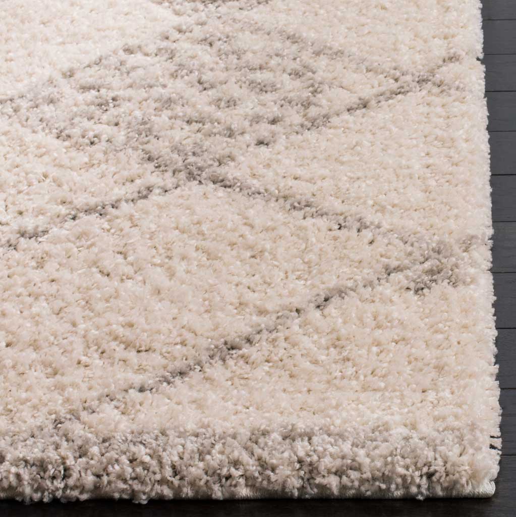 Plush ivory and gray fibers soften the rug's patterned edge and bound corner.