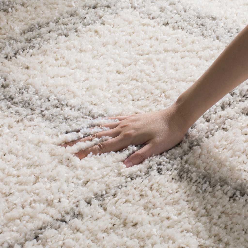 A hand presses into lofty ivory pile beside soft gray lines, highlighting its texture.