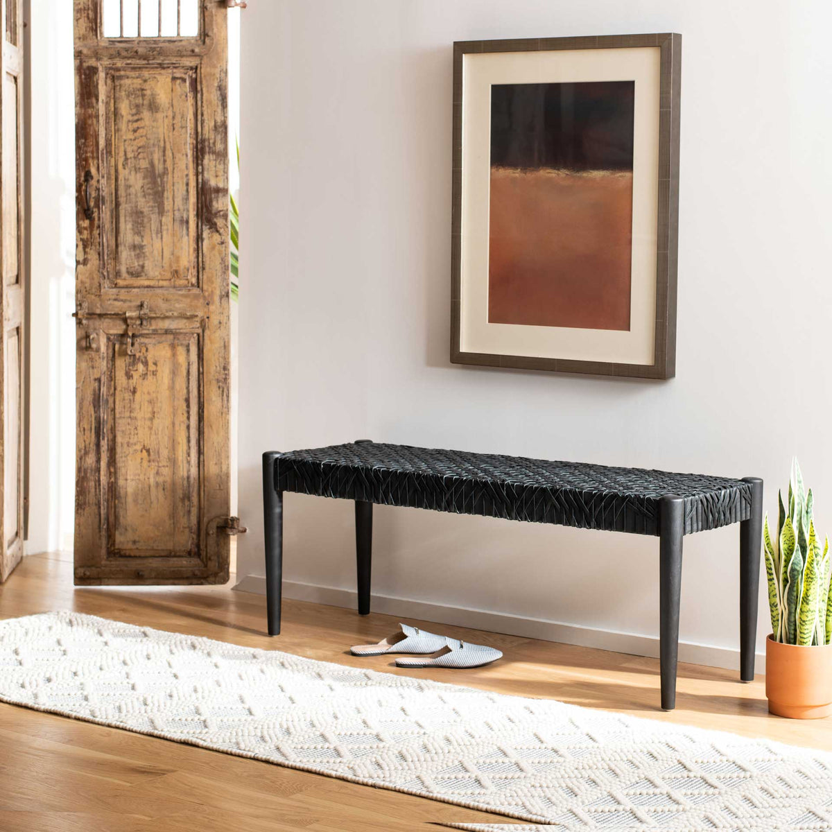 A black leather-weave bench adds crisp texture beside a weathered wood doorway.