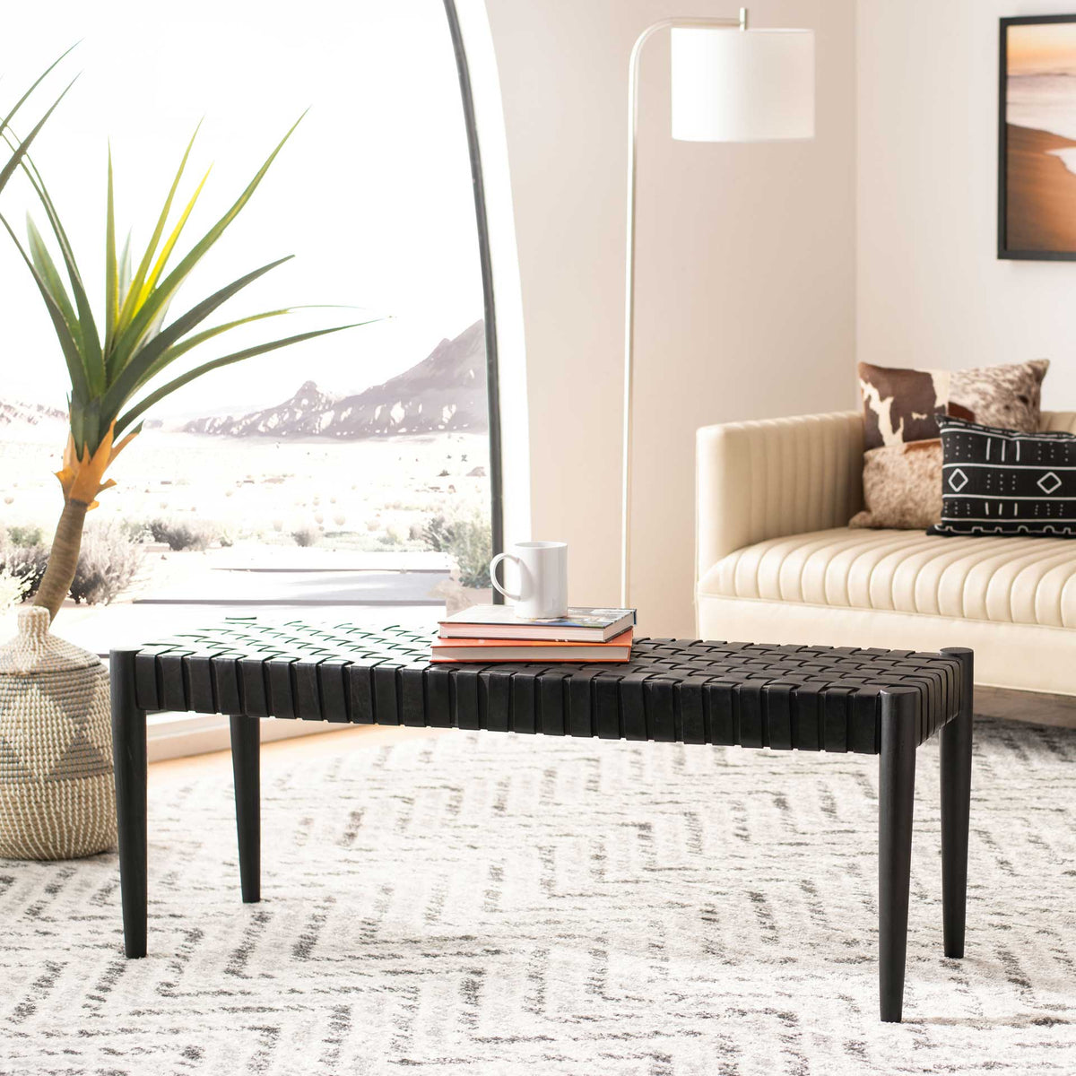 A black woven leather bench balances a textured seat on slender wood legs.