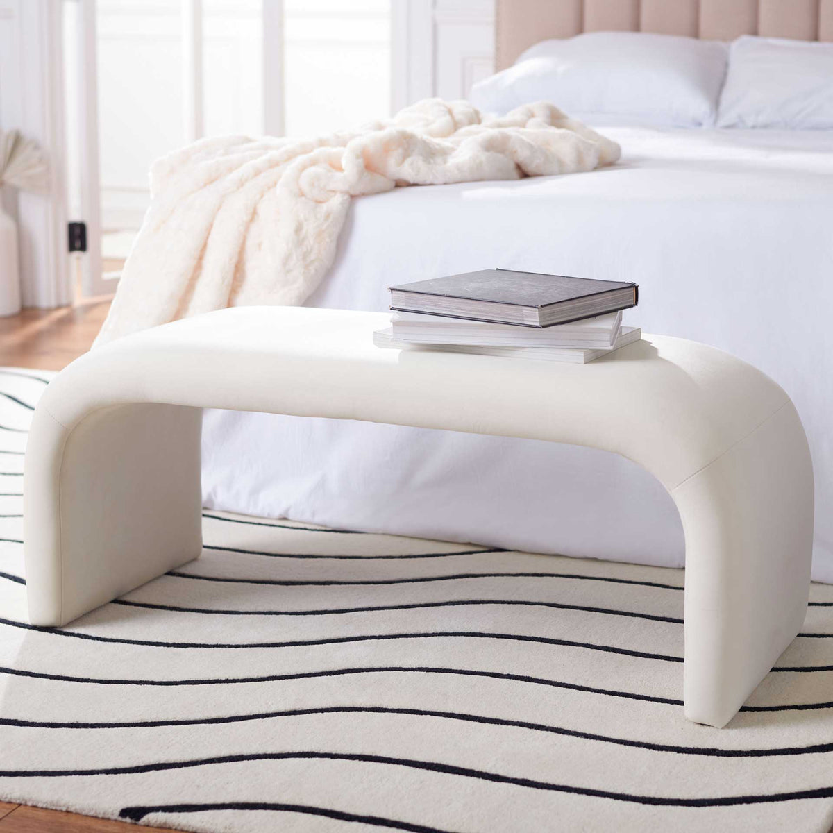 A cream velvet bench offers a soft, sculptural accent at the foot of a bed.