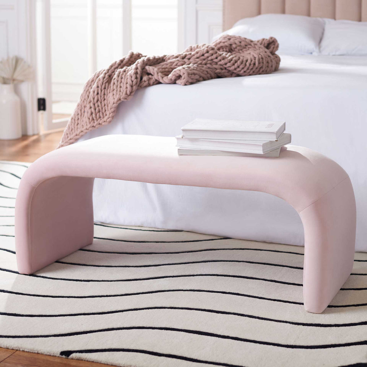 A light pink velvet bench adds a gentle accent at the foot of a bed.