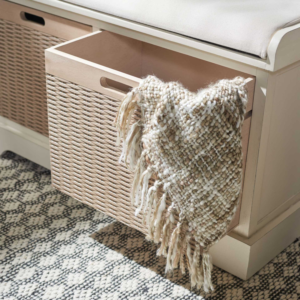 A spacious pullout basket stows a soft throw below the white cushioned seat.