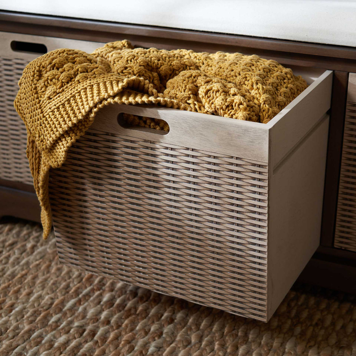 A deep woven drawer slides out to hold a chunky throw below the upholstered seat.