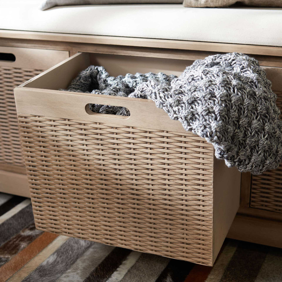 A roomy woven basket drawer holds a folded throw beneath the cushioned seat.