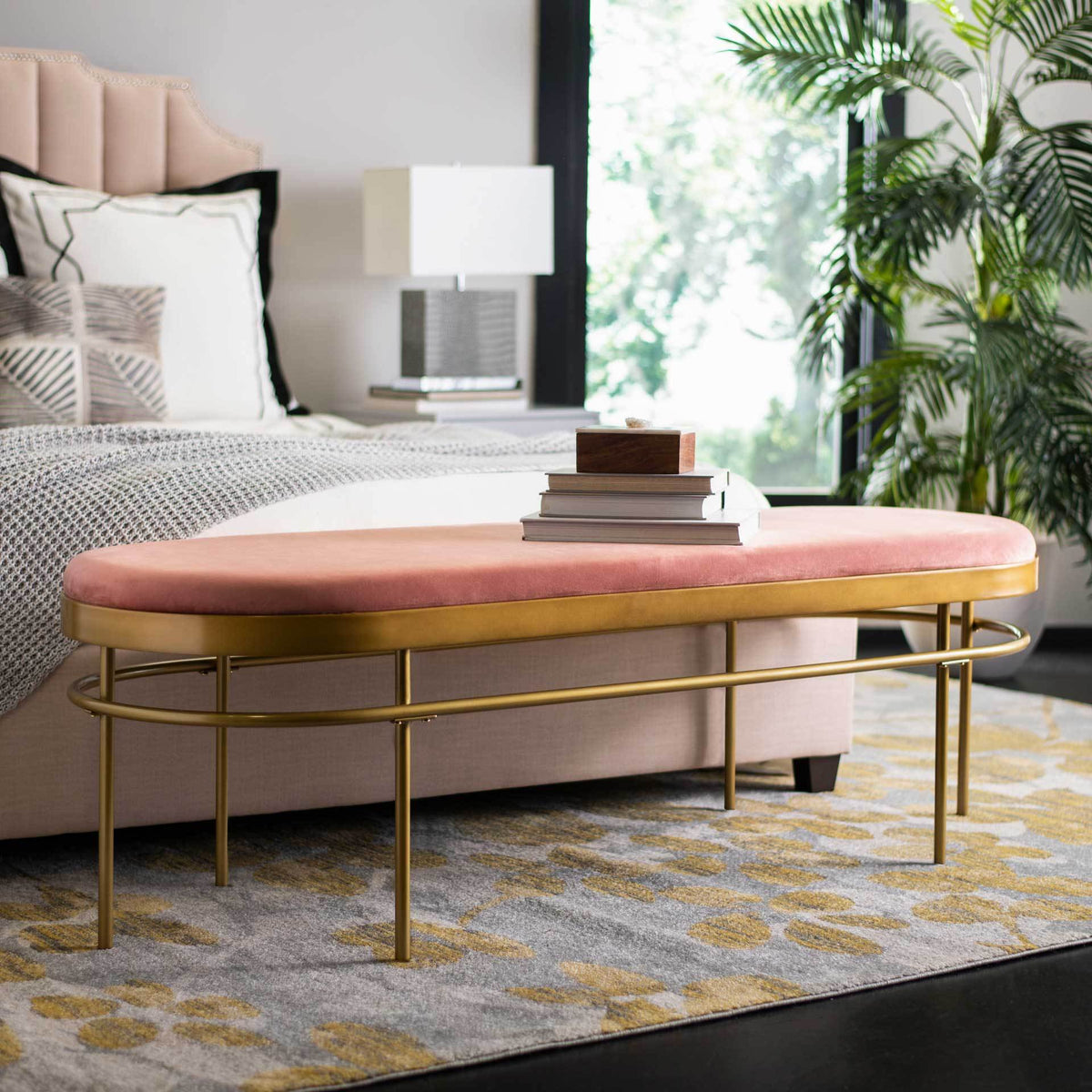 An elongated dusty rose velvet bench adds soft color and a touch of gold at the foot of a bed.