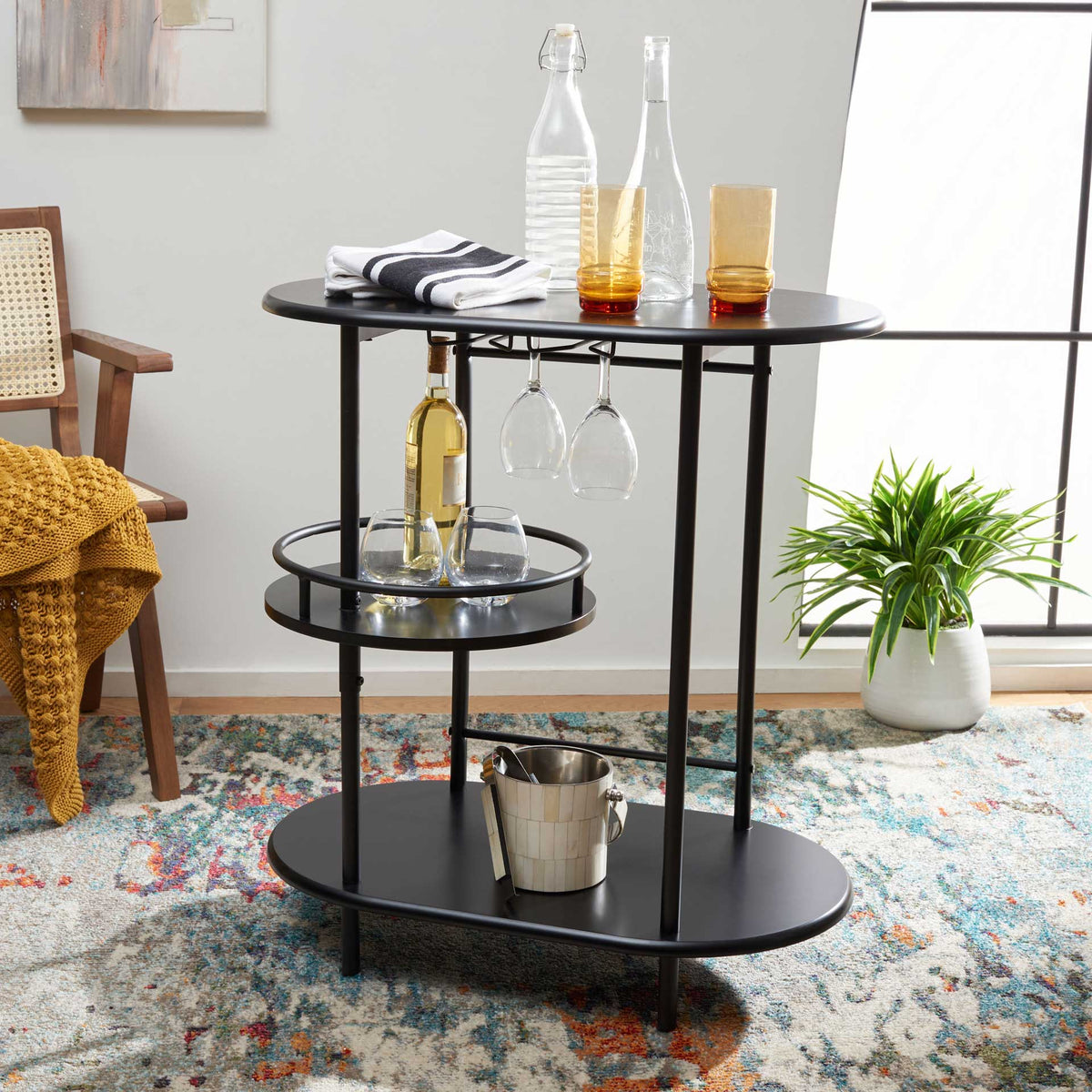 A matte black bar table keeps bottles, stemware, and serving essentials organized on three tiers.