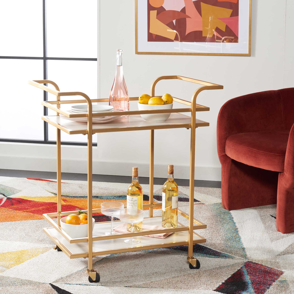 Matte gold bar cart displays drinks and fruit on two gray shelves behind protective rails.