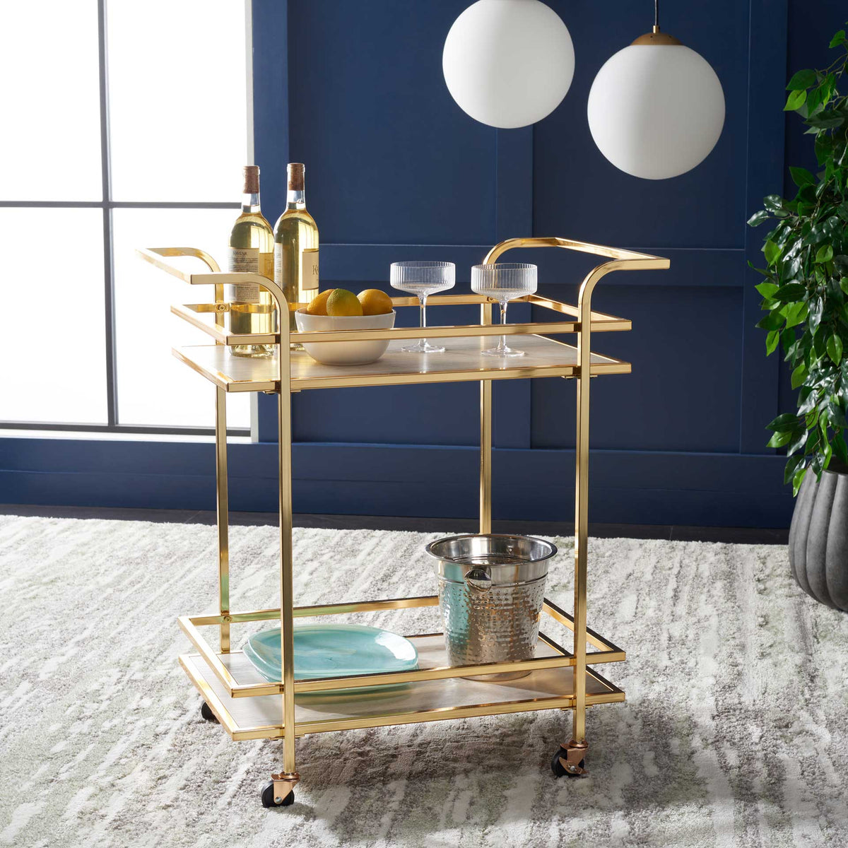 Polished gold cart serves drinks on two gray shelves, with rails to keep glassware in place.