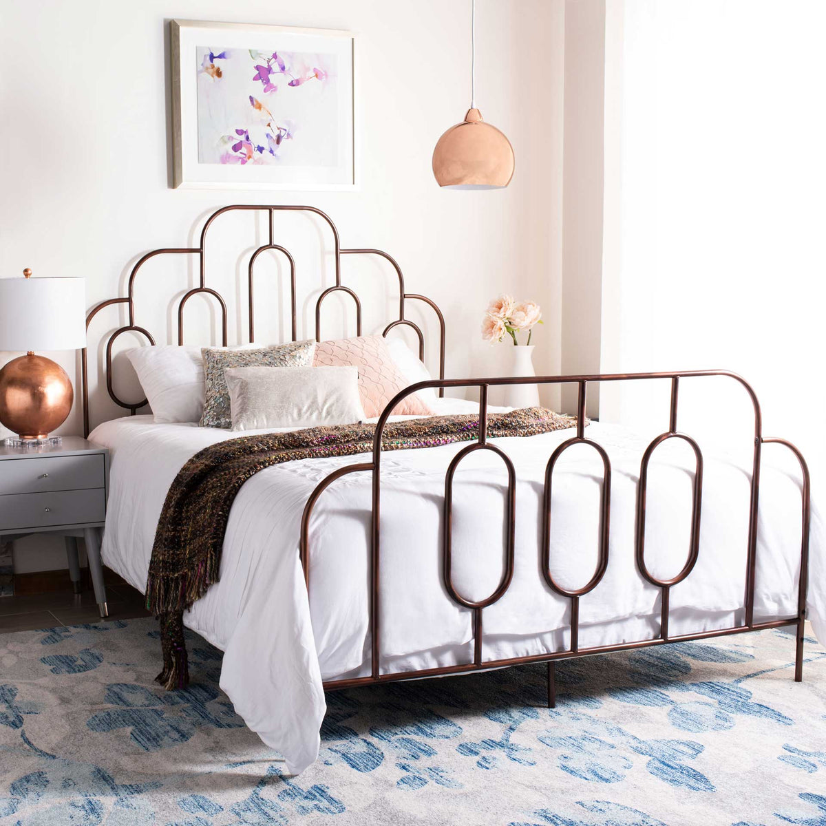 Antique bronze metal bed brings sculptural curves and oval accents to a layered bedroom