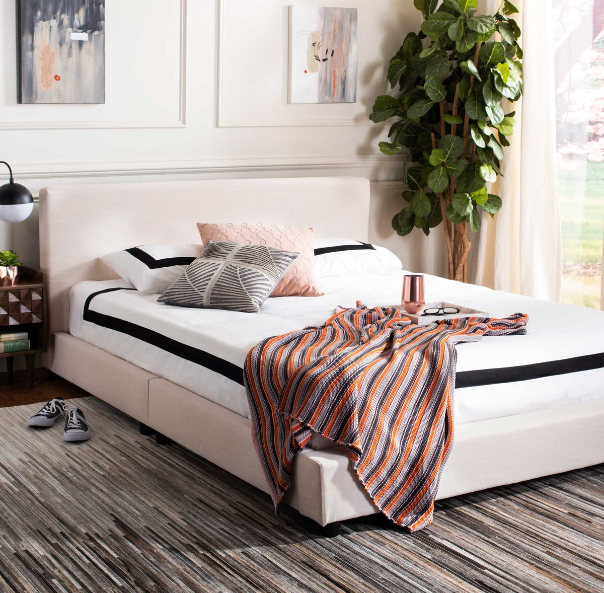 A light beige upholstered bed has a broad, understated headboard and a sleek low frame