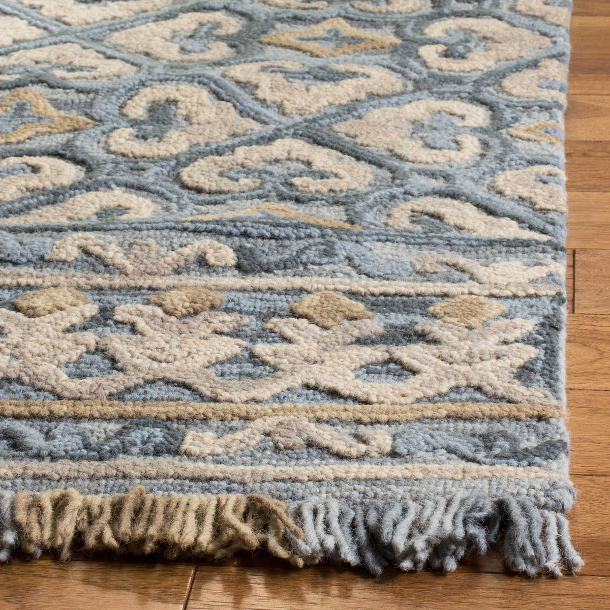 Textured blue and beige scrollwork meets geometric borders and soft, two-tone fringe.