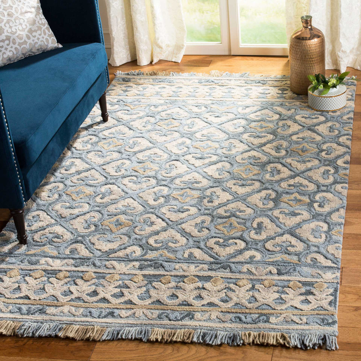Muted blue scrollwork and light beige accents lend soft pattern and fringed detail to a cozy seating area.
