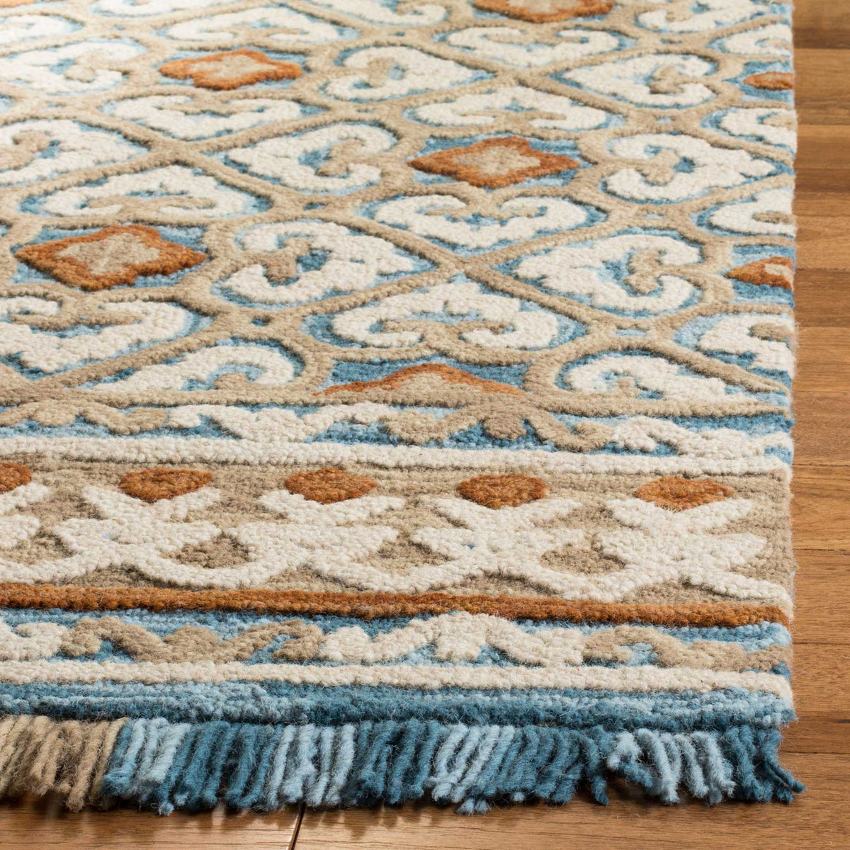Plush ivory and blue motifs meet a rust-accented border and a row of richly colored fringe.