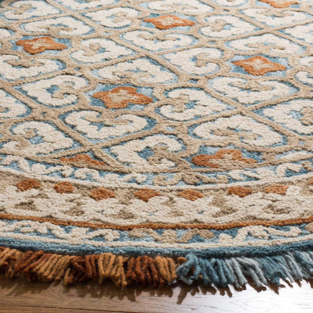 Textured ivory pile reveals blue scrollwork, rust motifs, and a colorful fringe