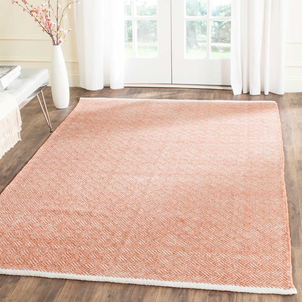 A bright orange and ivory herringbone rug warms wood floors with woven texture and white edging.