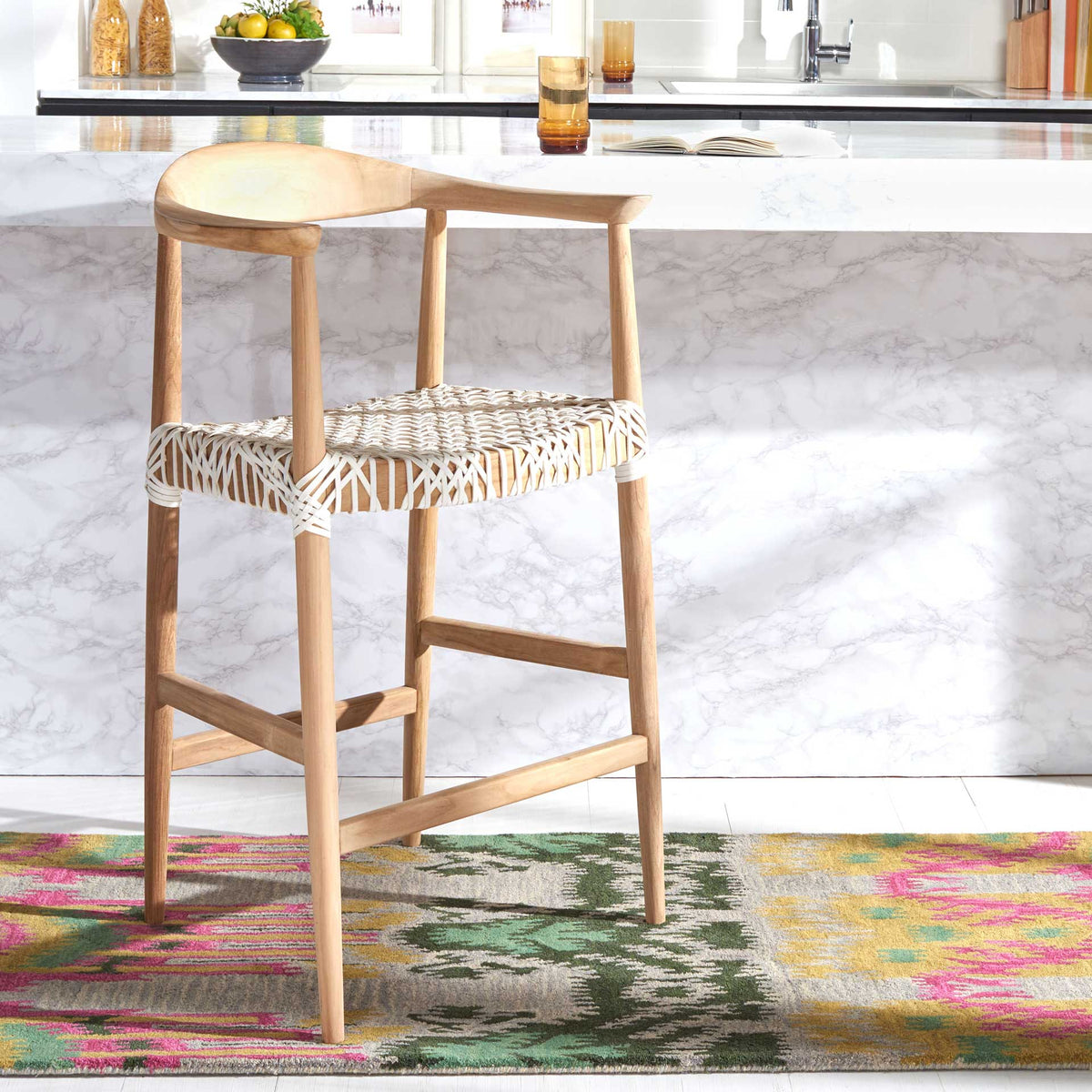 A curved teak back and crisp white leather weave add organic warmth beside a marble kitchen counter
