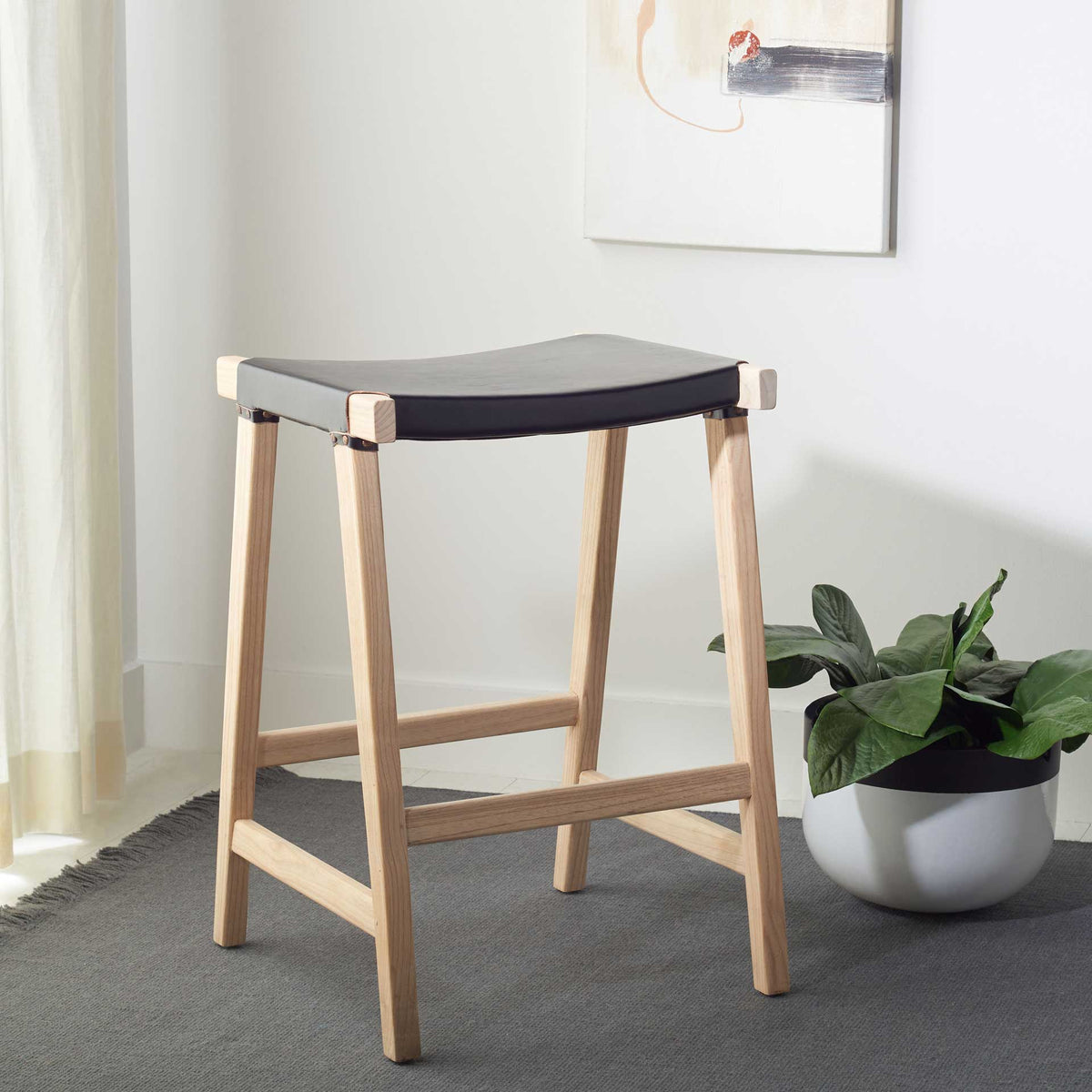 A streamlined counter stool pairs a black leather seat with warm, pale wood and an open frame