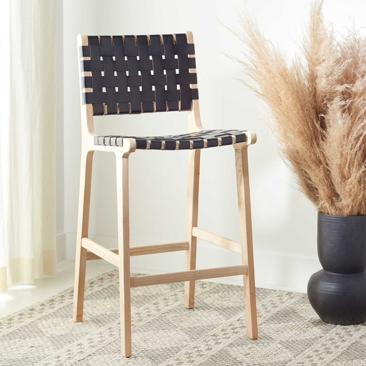 A black leather counter stool brings modern texture and natural wood warmth to a softly furnished space.