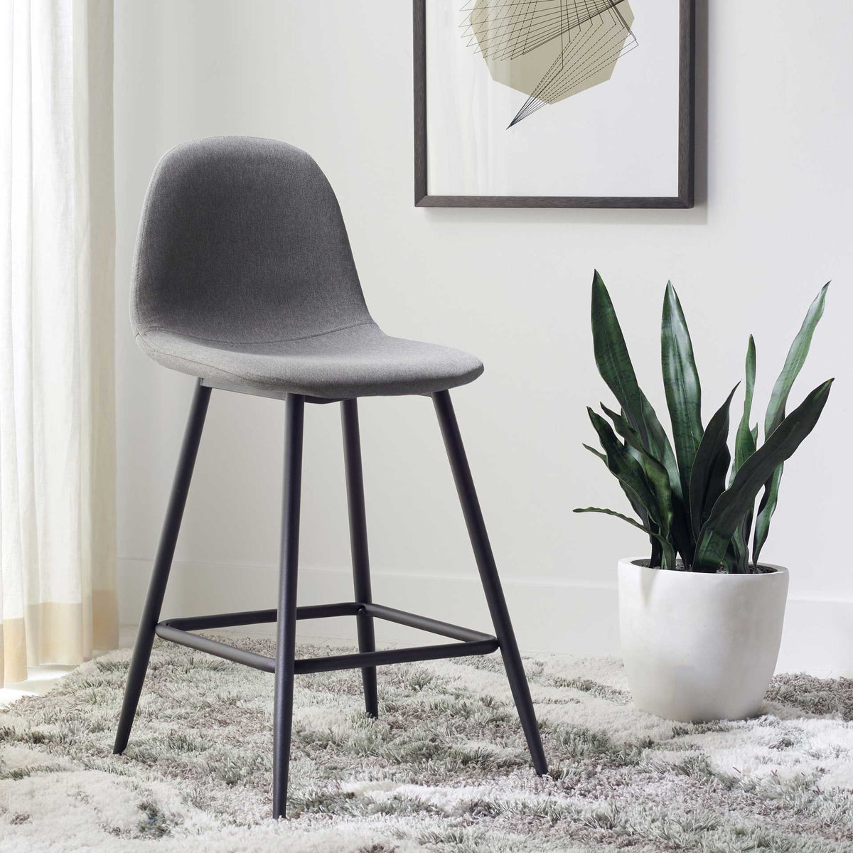 Soft gray upholstery and slender black legs lend modern style beside a potted plant