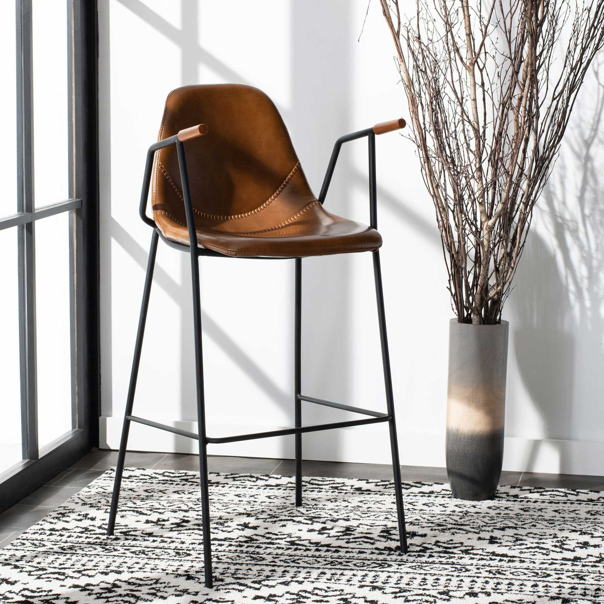 Cognac faux leather barstool features contrast stitching, slender black legs and wood-tipped arms